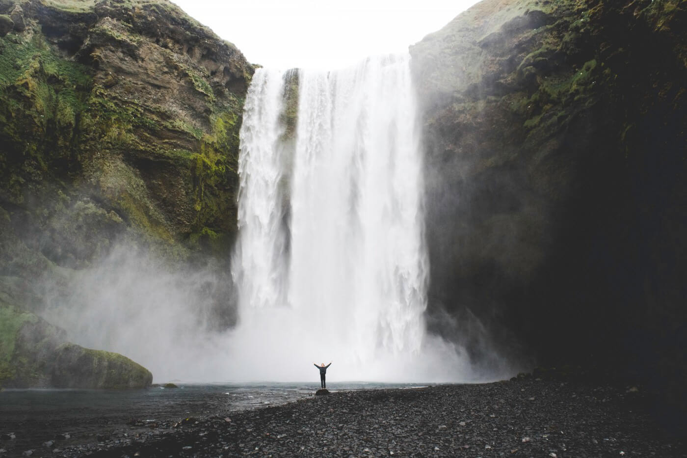 A huge waterfall in the background and a small figure standing at the bottom, raising their arms.